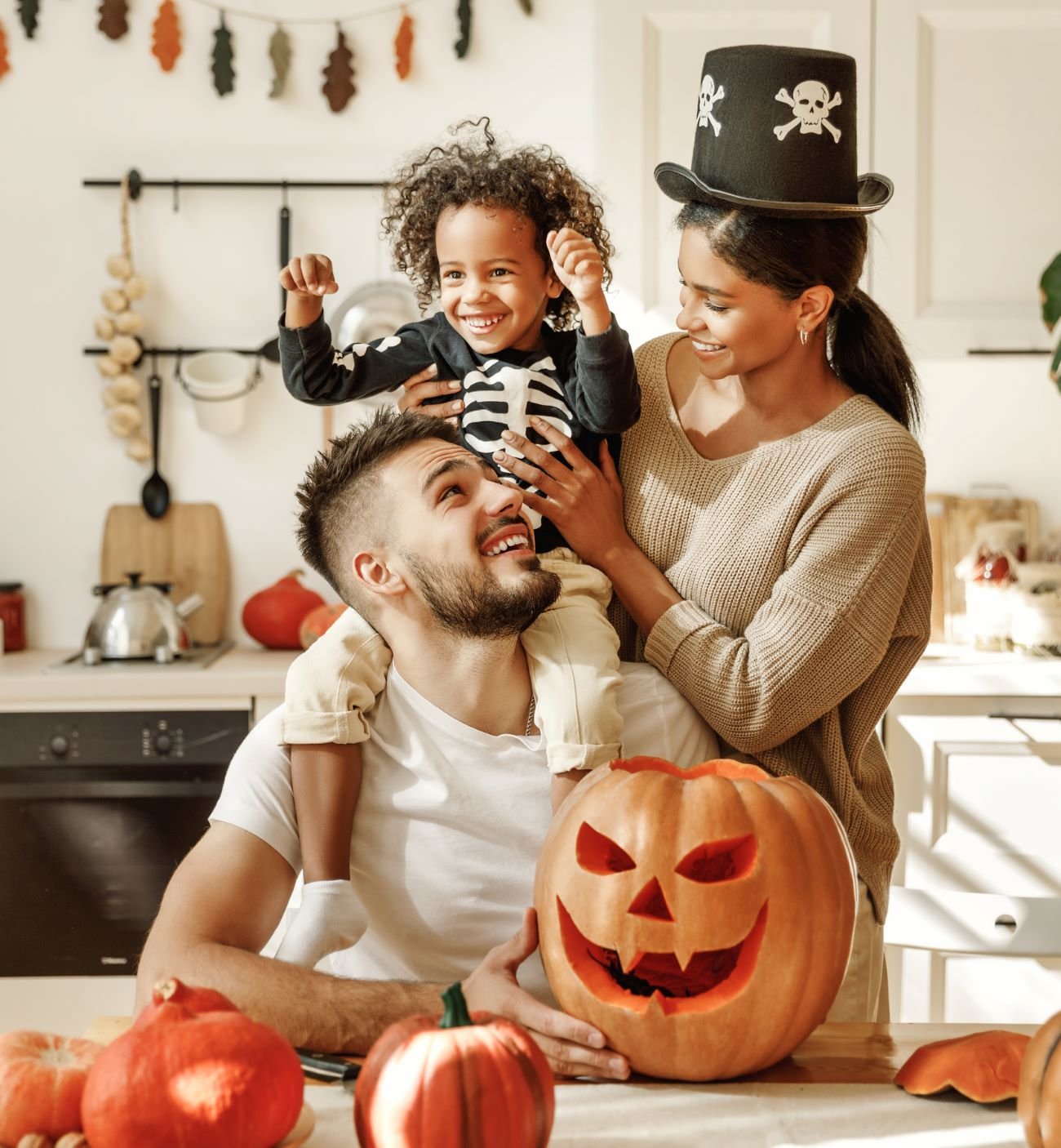 A family in their kitchen, parents and child gathered around a table, happily carving pumpkins for Halloween.