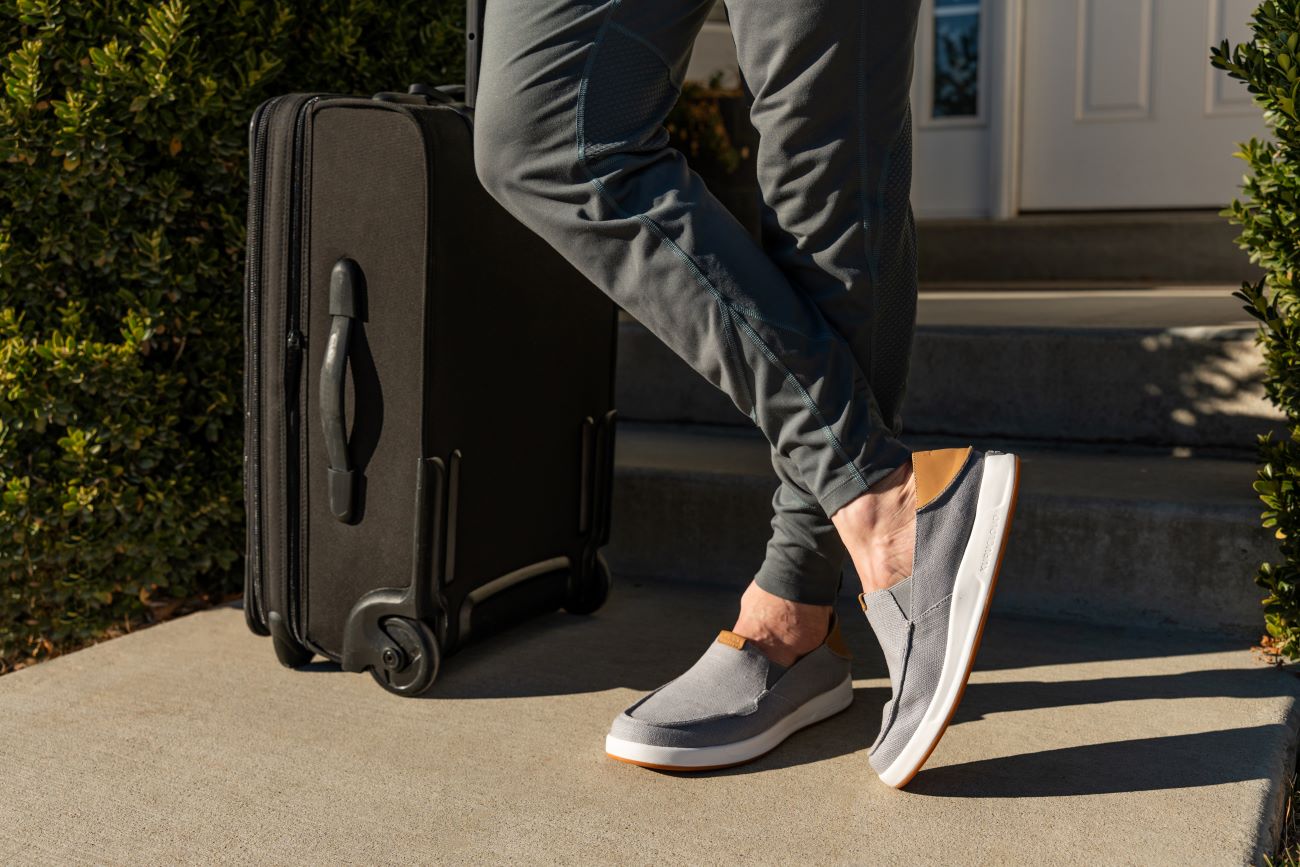 Man stands next to suitcase wearing KURU traveling shoes.