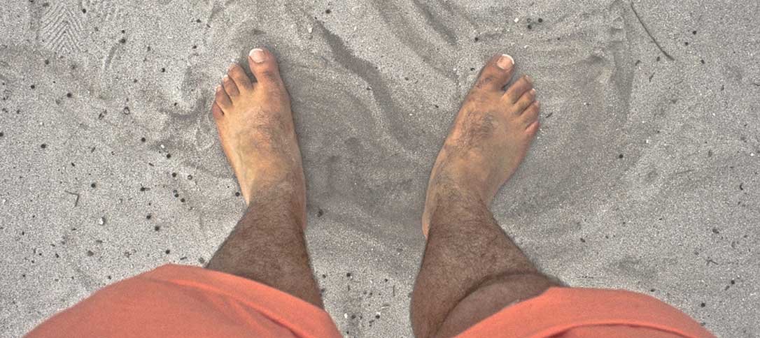 Man with foot disorder symptoms standing in sand on the beach.