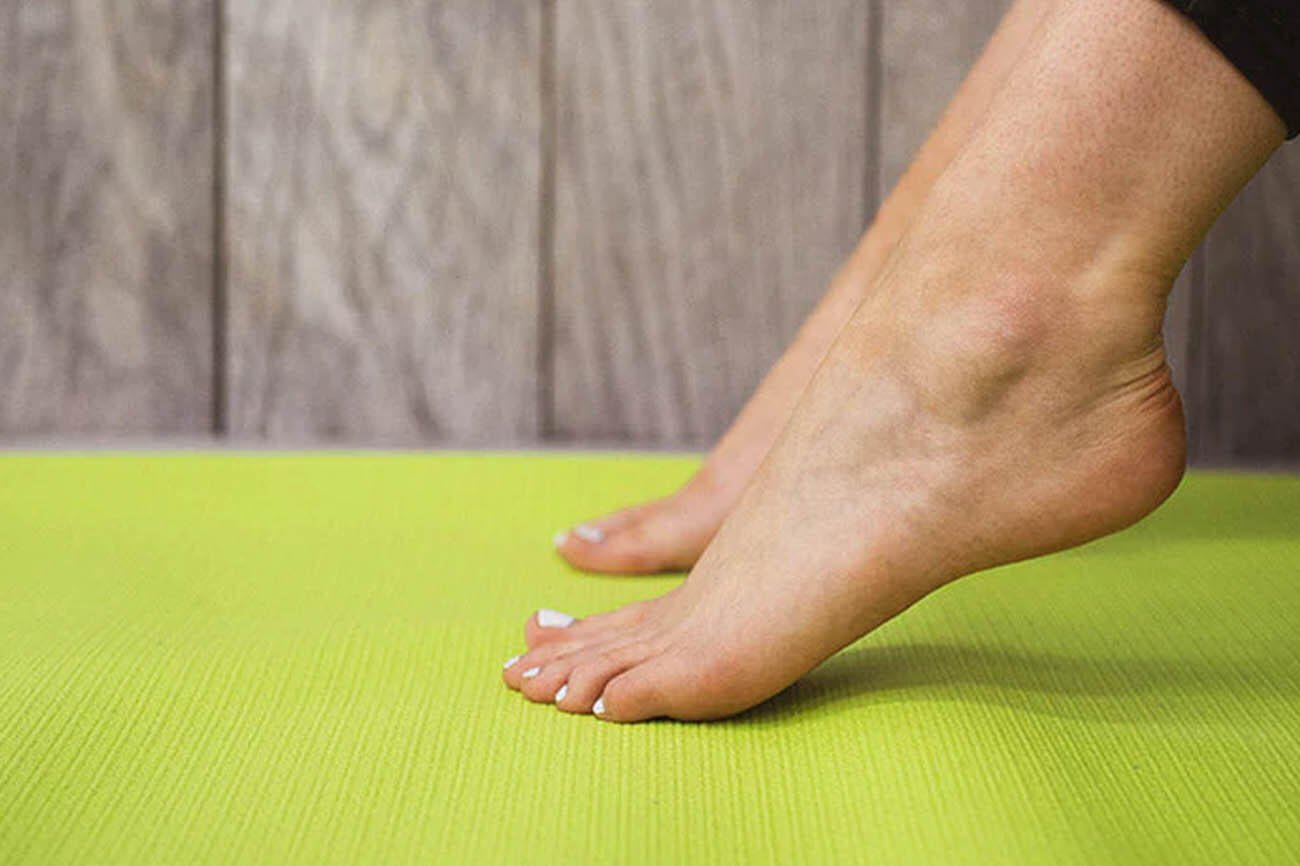 femme qui s'étend des pieds et des chevilles sur un tapis de yoga