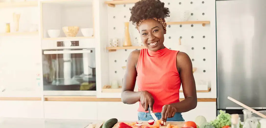 Smiling woman in a kitchen while cutting vegetables to prepare a meal.