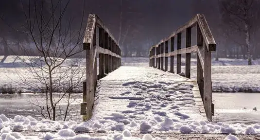 footprints along snow covered wooden bridge